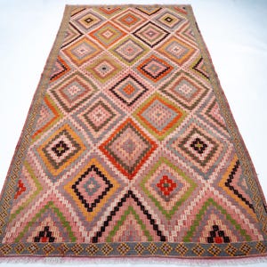 May include: A rectangular rug with a geometric diamond pattern. The rug features a variety of colors, including pink, orange, green, brown, and gray. The diamond pattern is repeated across the rug's surface, creating a visually appealing design. The rug has a fringed edge.
