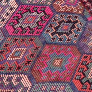 May include: A woven textile rug featuring a repeating geometric pattern of interconnected hexagons. The design incorporates a vibrant color palette of hot pink, deep blue, forest green, and muted brown, with intricate cross-stitch style detailing.
