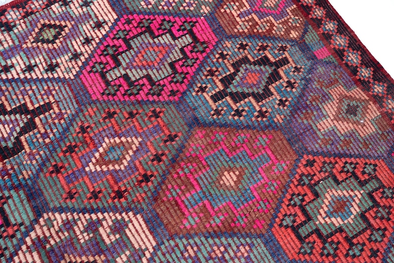 May include: A woven textile rug featuring a repeating geometric pattern of interconnected hexagons. The design incorporates a vibrant color palette of hot pink, deep blue, forest green, and muted brown, with intricate cross-stitch style detailing.