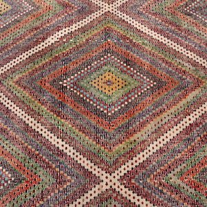 May include: A vibrant, geometric patterned rug with a diamond design. The rug features a variety of colours including red, green, orange, and white. The rug has a fringed edge.
