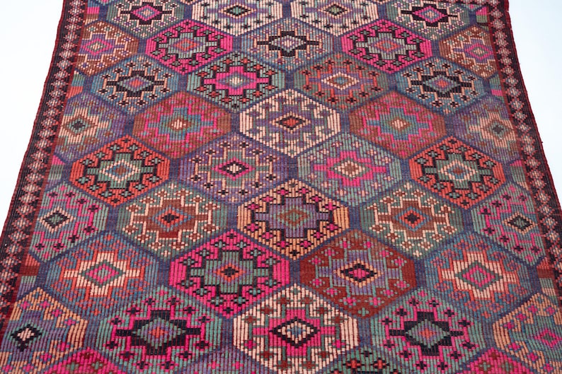 May include: A woven rug featuring a repeating geometric pattern of interconnected diamonds and octagons. The design incorporates a vibrant color palette of hot pink, deep purple, teal, orange, and black, with intricate small-scale cross-stitch details.