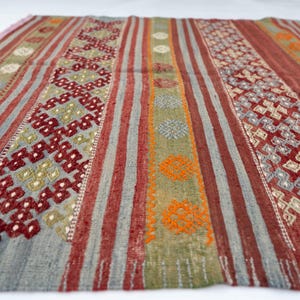 May include: A rectangular rug with a striped pattern in shades of red, gray, green, and orange. The rug features geometric designs and a fringed edge. The rug is made of woven fabric.