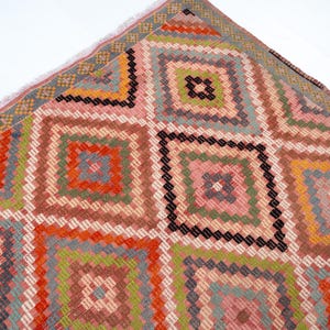 May include: A colorful, geometric patterned rug with a diamond design. The rug features squares within squares in shades of pink, orange, green, and brown. The edges have a fringe detail.