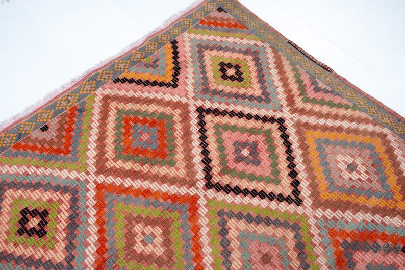 May include: A colorful, geometric patterned rug with a diamond design. The rug features squares within squares in shades of pink, orange, green, and brown. The edges have a fringe detail.