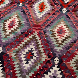 Puede incluir: Una colorida alfombra con dise&ntilde;o geom&eacute;trico y patr&oacute;n de diamantes. La alfombra presenta una variedad de colores, incluyendo rojo, morado, verde y blanco. La alfombra est&aacute; hecha de un material tejido y tiene una apariencia texturizada.