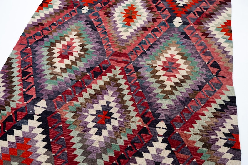 Puede incluir: Una colorida alfombra con dise&ntilde;o geom&eacute;trico y patr&oacute;n de diamantes. La alfombra presenta una variedad de colores, incluyendo rojo, morado, verde y blanco. La alfombra est&aacute; hecha de un material tejido y tiene una apariencia texturizada.