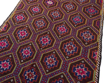 May include: A woven rug featuring a repeating geometric pattern of dark brown hexagons. Each hexagon contains a central eight-pointed star in shades of magenta, blue, and white, outlined by thin yellow and orange borders with small white dots.