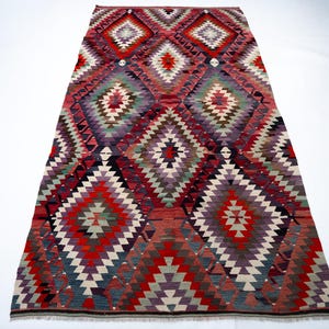 Puede incluir: Una alfombra rectangular tejida a mano con un patr&oacute;n geom&eacute;trico de diamantes. La alfombra presenta una vibrante paleta de colores de rojo, morado, verde y blanco. El dise&ntilde;o es sim&eacute;trico, con formas de diamantes repetidas. Esta alfombra es adecuada para la decoraci&oacute;n del hogar.