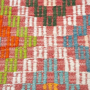 May include: Close-up of a woven textile with a colorful, geometric pattern. The design features alternating blocks of red, white, green, orange, and blue. The texture appears soft and the weave is tight.