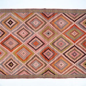 May include: Rectangular rug with a geometric diamond pattern. The rug features a repeating pattern of diamonds in shades of pink, orange, green, gray, and black. The border is a darker shade of gray with a repeating pattern.