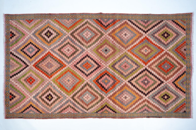 May include: Rectangular rug with a geometric diamond pattern. The rug features a repeating pattern of diamonds in shades of pink, orange, green, gray, and black. The border is a darker shade of gray with a repeating pattern.