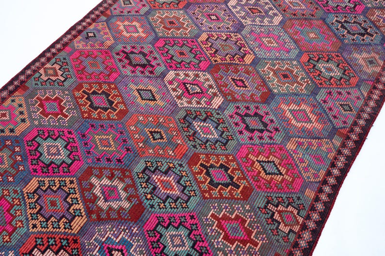 May include: A rectangular woven rug featuring a repeating geometric pattern of interconnected diamonds and hexagons. The design incorporates a vibrant color palette of hot pink, deep purple, teal, orange, and dark red, finished with a dark border.