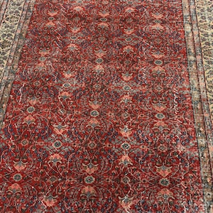 May include: A rectangular area rug featuring a deep red field covered in a repeating intricate floral and vine pattern in shades of blue, cream, and pink. The rug is framed by a wide border with a dense, multi-colored botanical motif.