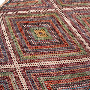 May include: A vibrant, geometric rug with a diamond pattern. The rug features a variety of colours, including red, green, blue, and yellow. The design is symmetrical, with a central diamond surrounded by other diamond shapes. The rug has a fringed edge.