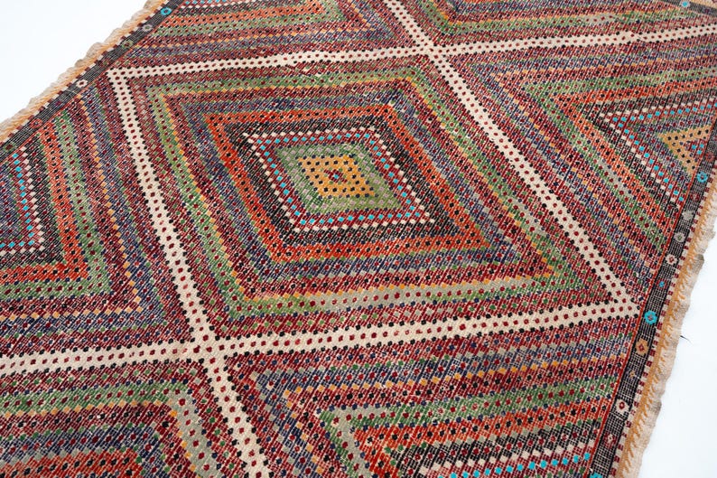 May include: A vibrant, geometric rug with a diamond pattern. The rug features a variety of colours, including red, green, blue, and yellow. The design is symmetrical, with a central diamond surrounded by other diamond shapes. The rug has a fringed edge.