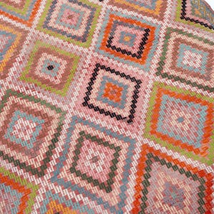 May include: Close-up of a colorful woven rug with a geometric diamond pattern. The rug features a variety of colors, including pink, orange, green, blue, and black. The design is intricate and detailed, with each diamond containing smaller squares.