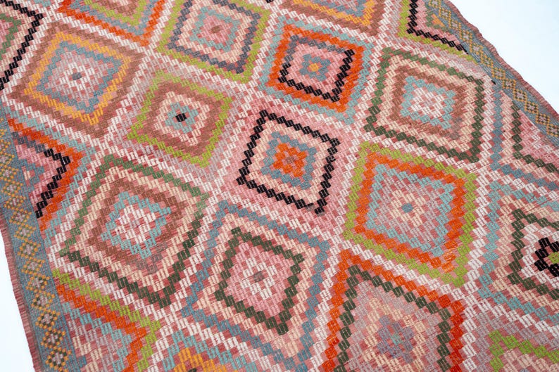 May include: Close-up of a colorful woven rug with a geometric diamond pattern. The rug features a variety of colors, including pink, orange, green, blue, and black. The design is intricate and detailed, with each diamond containing smaller squares.