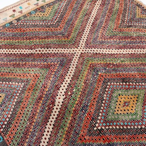 May include: A vibrant, geometric patterned rug with a diamond design. The rug has a cream-coloured border with small, colourful embroidered details. The main body of the rug showcases a series of diamond shapes in shades of red, green, orange, and blue.