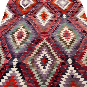 Puede incluir: Una alfombra colorida con un dise&ntilde;o geom&eacute;trico y un dise&ntilde;o de diamantes. La alfombra presenta una variedad de colores, incluyendo rojo, morado, verde y blanco. La alfombra est&aacute; hecha de material tejido y es adecuada para la decoraci&oacute;n del hogar.