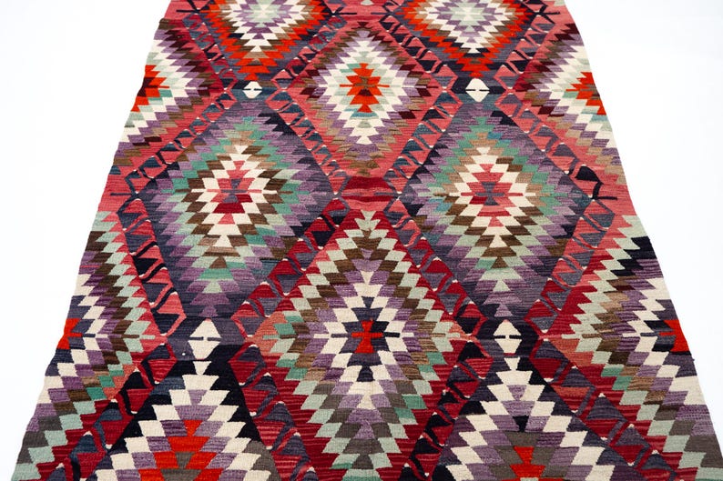 Puede incluir: Una alfombra colorida con un dise&ntilde;o geom&eacute;trico y un dise&ntilde;o de diamantes. La alfombra presenta una variedad de colores, incluyendo rojo, morado, verde y blanco. La alfombra est&aacute; hecha de material tejido y es adecuada para la decoraci&oacute;n del hogar.