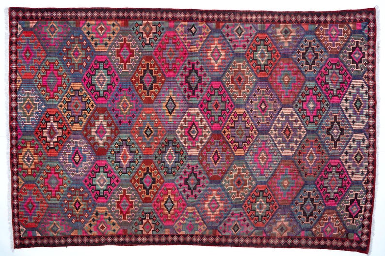 May include: A rectangular woven rug featuring a repeating diamond pattern in vibrant shades of magenta, purple, teal, orange, and black. The design includes intricate geometric motifs within each diamond shape, framed by a dark maroon border.