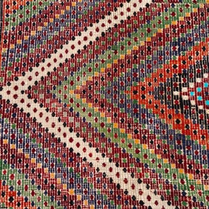 May include: Close-up of a colourful, patterned rug with a geometric design. The rug features a variety of colours including red, green, blue, orange, and white. The edges have a fringed border.