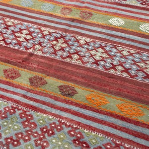 May include: A colorful rug with a geometric pattern. The rug features alternating stripes of red, blue, and green, with diamond and floral motifs. The rug's design incorporates various shades of red, blue, green, and orange.