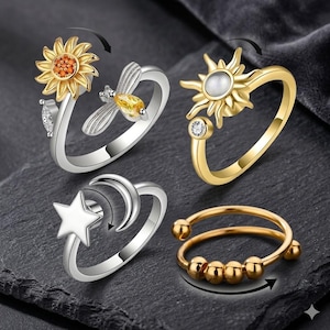Puede incluir: Se muestran cuatro anillos giratorios. Uno tiene un diseño de girasol, otro un sol con un centro de perla, un tercero una estrella y una luna creciente, y el último tiene cuentas doradas. Los anillos son plateados y dorados.