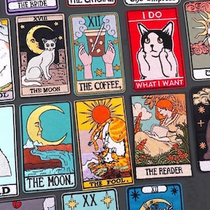 Può includere: Toppe ricamate di carte dei tarocchi con vari disegni. Le carte includono "The Moon" con un gatto, "The Coffee" con una bevanda e "What I Want" con un gatto. Altre carte mostrano "The Fool" e "The Reader".