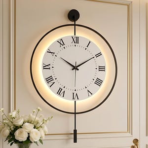 Könnte beinhalten: Eine moderne Wanduhr mit weißem Zifferblatt, schwarzen römischen Ziffern und schwarzen Zeigern. Die Uhr ist von einem schwarzen kreisförmigen Rahmen mit einem leuchtenden Licht umgeben. Ein schwarzes Pendel hängt darunter. Die Uhr ist an einer weißen Wand befestigt.