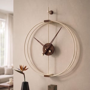Può includere: Un orologio da parete moderno con una cornice circolare color crema e lancette marrone scuro. L'orologio è montato su una parete beige sopra una consolle in legno. Gli oggetti decorativi includono un vaso nero con un fiore e sculture geometriche in bronzo.