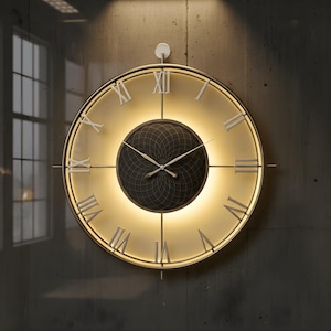 Puede incluir: Un reloj de pared grande y redondo con un marco dorado y una esfera color crema. El reloj presenta números romanos y un centro negro con dibujos. El reloj está iluminado con una luz cálida y suave.