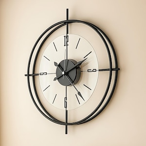 May include: A modern wall clock with a clear glass face and black metal frame. The clock features black hands and minimalist hour markers. The design includes a circular frame with intersecting vertical and horizontal bars.