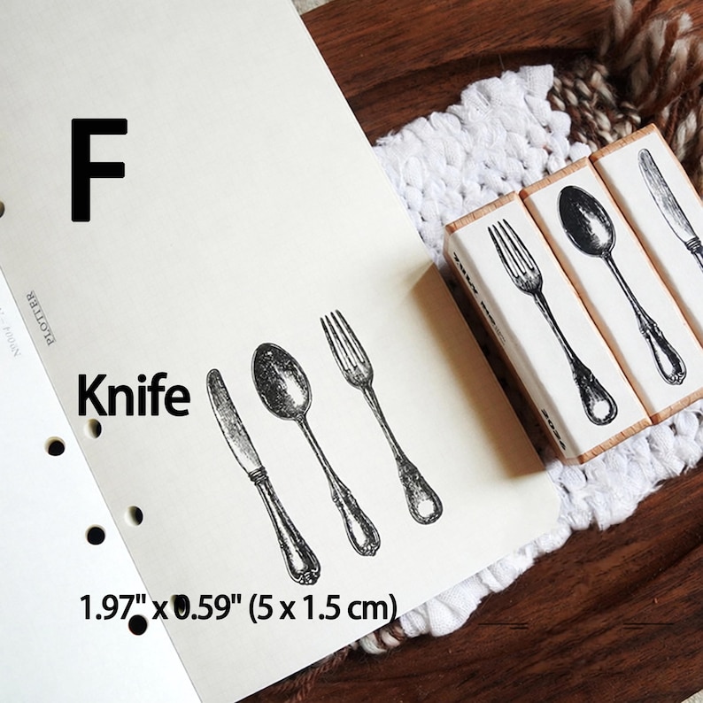May include: Three rectangular wooden stamps featuring detailed black ink illustrations of a knife, a spoon, and a fork. The stamps are labeled with the letter F and the word Knife, with dimensions of 1.97 inches by 0.59 inches printed on the paper.