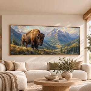May include: A panoramic wall art print featuring a brown bison standing on a grassy hillside. The background displays a vast mountain range with snow-capped peaks, green valleys, and dense pine forests under a soft, light-filled sky.
