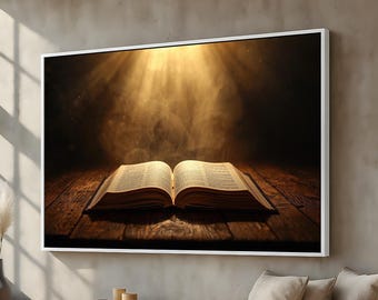 May include: A framed print of an open book on a wooden surface, illuminated by a beam of light. The pages are visible, and the background is dark and smoky. The frame is white, and the overall aesthetic is warm and inviting.