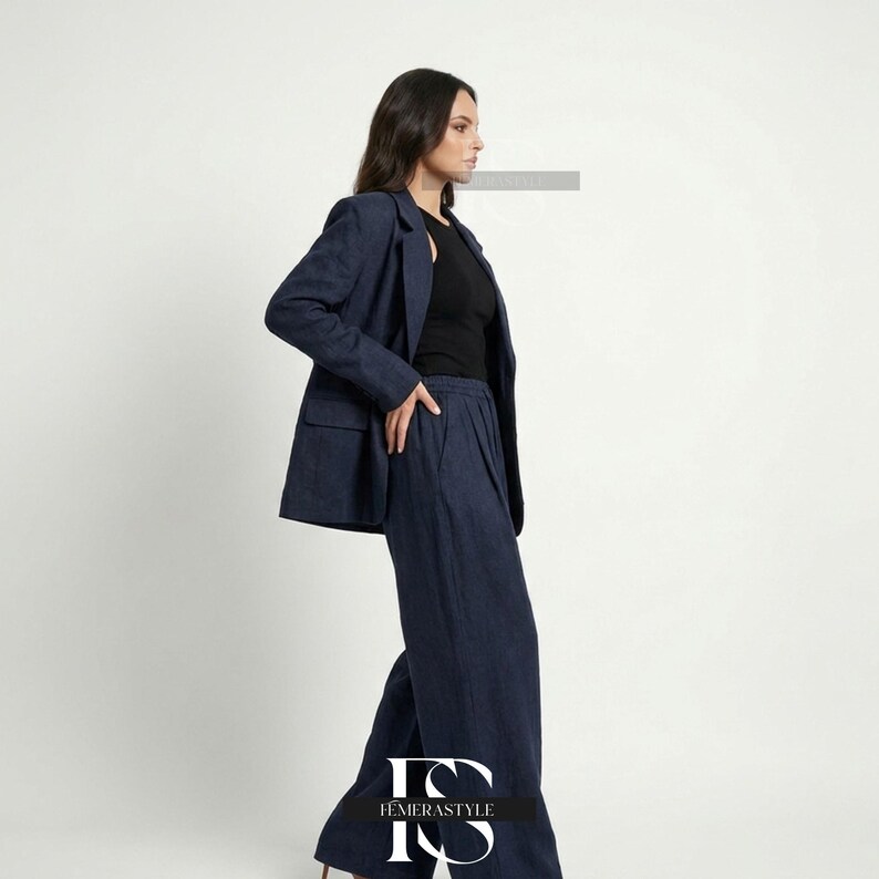 May include: A dark blue blazer and matching wide-leg trousers set worn over a black sleeveless top. The blazer features notched lapels and two front pockets. The trousers have a high-waisted fit with a pleated front design and a loose silhouette.