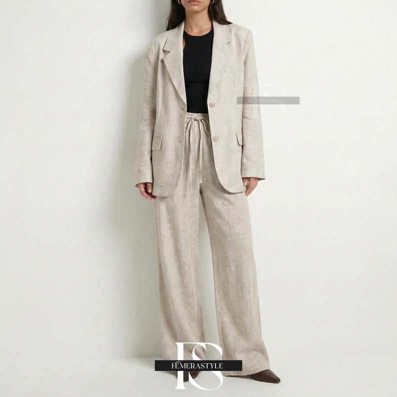 May include: A beige blazer and matching wide-leg trousers set featuring a textured fabric. The blazer has notched lapels, two front buttons, and flap pockets. The trousers include a drawstring waist. A black sleeveless top is worn underneath.