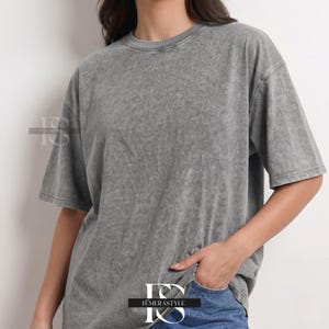 Pu&ograve; includere: Una maglietta grigia con lavaggio acido, a maniche corte e girocollo. La maglietta ha una vestibilit&agrave; leggermente oversize e un aspetto strutturato. L'indumento &egrave; abbinato a jeans blu. Il marchio "IEMERASTYLE" &egrave; visibile.