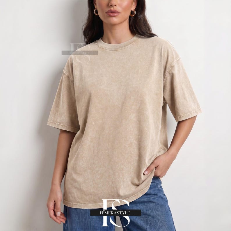 Pu&ograve; includere: Una maglietta beige oversize con girocollo e maniche corte. La maglietta ha un aspetto sbiadito e strutturato. La modella indossa jeans blu. La maglietta &egrave; del marchio "IEMERASTYLE".