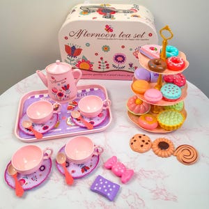 Op de afbeelding: Een roze en paarse speelgoed theeset met een draagtas, theepot, kopjes, schotels, lepels en een etagère. De set bevat speelgoedkoekjes, snoepjes en gebakjes. De draagtas heeft de tekst "Afternoon tea set".