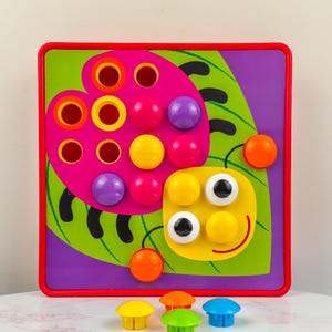Può includere: Un giocattolo in legno colorato con un design a coccinella, con una tavola e pioli. La tavola ha una cornice rossa, una foglia verde e uno sfondo viola. Include pioli gialli, arancioni, verdi e blu.