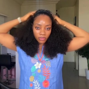 May include: A light blue sleeveless top with floral embroidery in shades of white, red, orange, and green. The top has a V-neck design. The person is wearing a bracelet on their wrist.