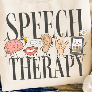 Puede incluir: Una sudadera color crema con el texto gris oscuro SPEECH THERAPY. El diseño incluye ilustraciones de dibujos animados de un cerebro, una bombilla, una boca, una oreja, una mano haciendo el signo de te quiero en lengua de signos y una tableta.