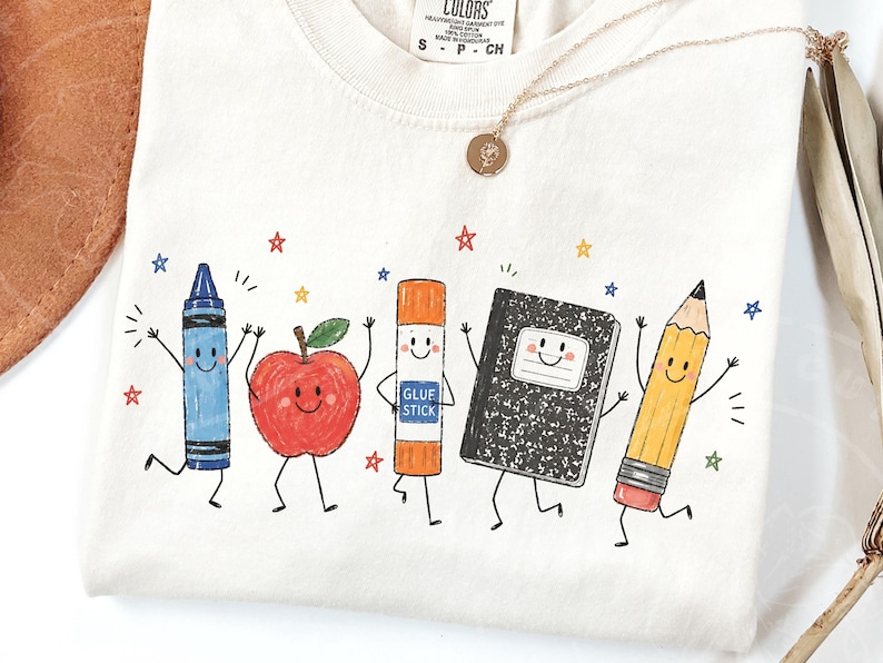 May include: Off-white t-shirt with a cheerful design of school supplies: a blue crayon, red apple, glue stick, notebook, and yellow pencil, each with a smiling face. The design includes colourful stars and the text "COLORS" on the upper left.