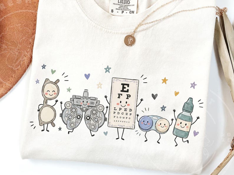 May include: A cream-colored t-shirt featuring a graphic print of five anthropomorphic eye care items: a pair of glasses, a phoropter, an eye chart with the letters E, F, P, L, P, E, D, P, D, C, Z, P, F, L, O, W, P, C, contact lens case, and eye drops.