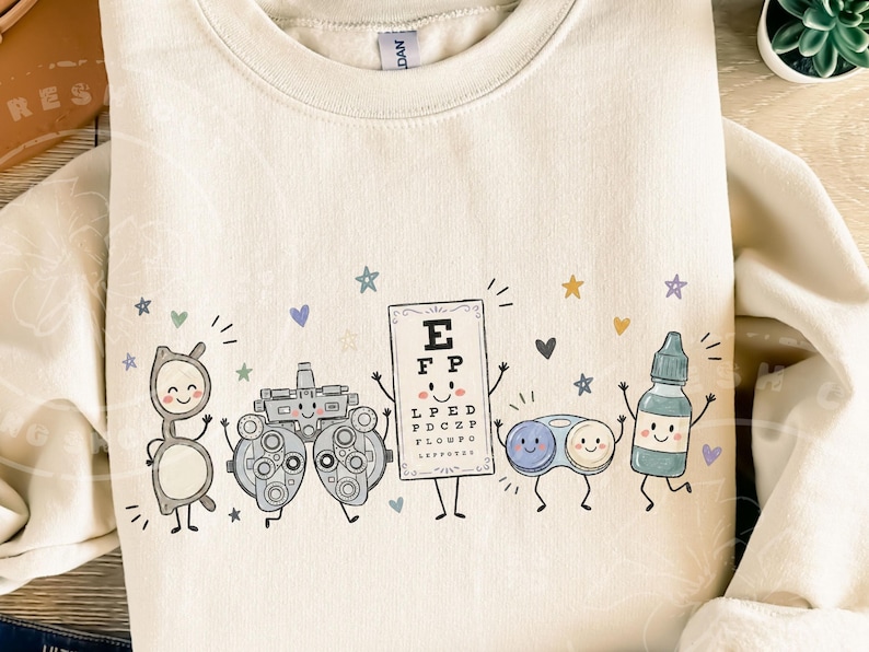 May include: A cream-colored crewneck sweatshirt featuring a graphic print of five anthropomorphic eye care items: a pair of glasses, a phoropter, an eye chart with the letters E, F, P, L, P, E, D, P, D, C, Z, P, F, L, O, W, F, O, a contact lens case, and an eye drop bottle.