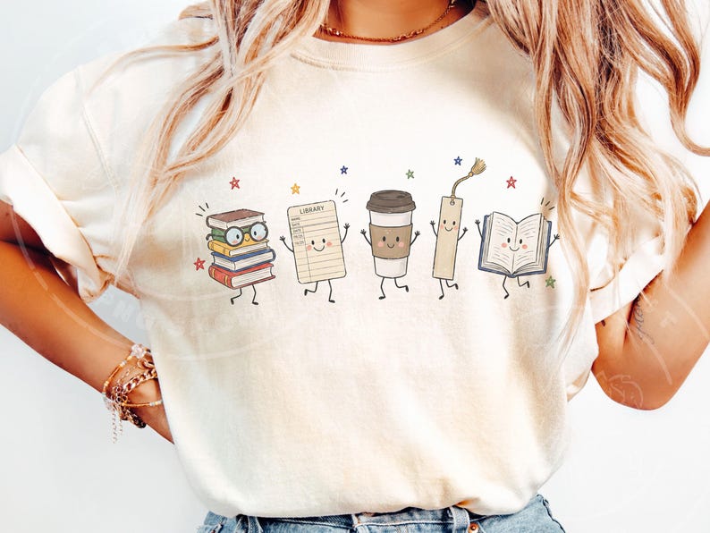 Pu&ograve; includere: Una t-shirt color crema con una stampa grafica di cinque personaggi antropomorfi: una pila di libri con occhiali, una scheda di biblioteca con la parola LIBRARY, un bicchiere di caff&egrave;, un segnalibro e un libro aperto, circondati da stelle.