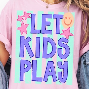 May include: A light pink t-shirt with the words "LET KIDS PLAY" in large, blue, bubble letters. The text is set against a background of vertical stripes in light blue and white. Pink stars and a smiling face graphic are also included.