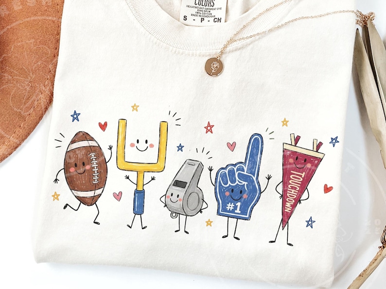 May include: An off-white t-shirt featuring a graphic print of five anthropomorphic football-themed characters: a brown football, a yellow goalpost, a grey whistle, a blue foam finger with the text #1, and a red pennant with the text TOUCHDOWN.